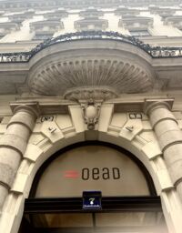 Facade of building with letters OEAD on window.